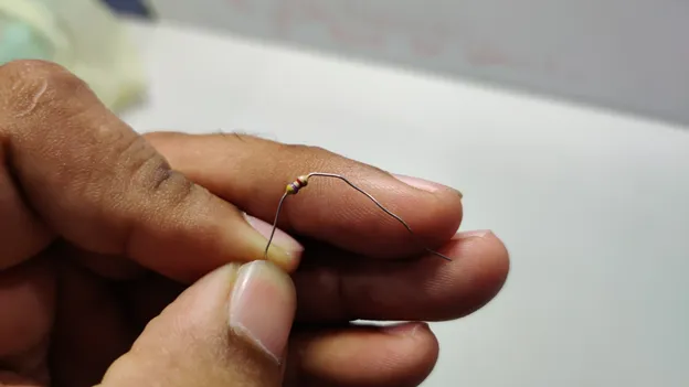 Hand holding a small resistor with its leads bent outward